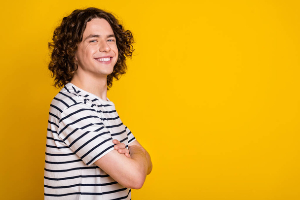 Photo of nice young man crossed arms empty space ad wear striped t-shirt isolated on yellow color background. - Photo, image