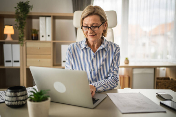 ώριμη γυναίκα επιχειρηματίας χρησιμοποιούν φορητό υπολογιστή κατά την εργασία στο γραφείο - Φωτογραφία, εικόνα
