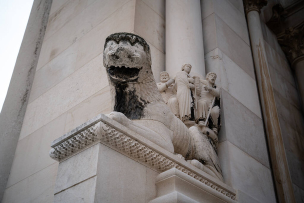 Kamienna rzeźba lwa, ze szczegółowymi figurami ludzkimi w tle, zdobi elegancki zabytkowy budynek.  - Zdjęcie, obraz