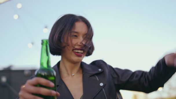 Gros plan asiatique fille danse avec boisson à terrasse disco. Joyeux jeune femme appréciant la fête avec bouteille de bière à la main. Détendu danseur ravi de s'amuser au divertissement sur le toit. Liberté concept jeunesse  - Photo, image
