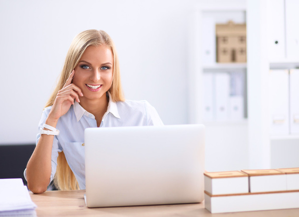 Ελκυστική επιχειρηματίας κάθεται σε ένα γραφείο με φορητό υπολογιστή στο γραφείο - Φωτογραφία, εικόνα