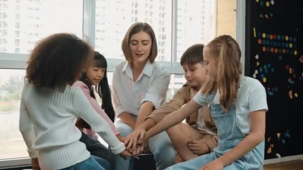 Teacher and diverse students putting hands together at classroom. Young instructor and multicultural children cheering and encourage. Represented unity, love, cooperate, working together. Erudition. - Footage, Video