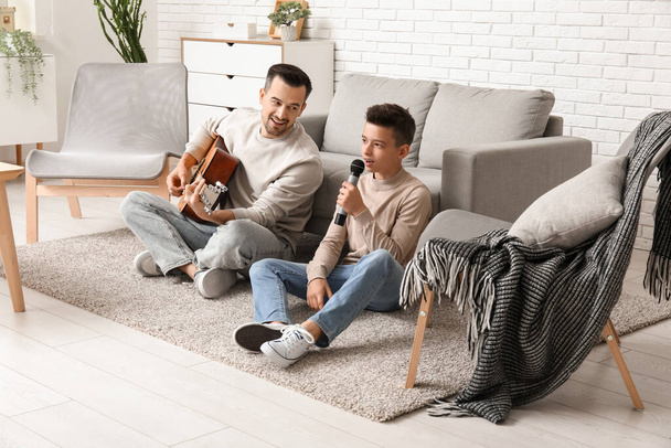 Baba ve küçük oğlu evde gitar çalıp şarkı söylüyorlar. - Fotoğraf, Görsel