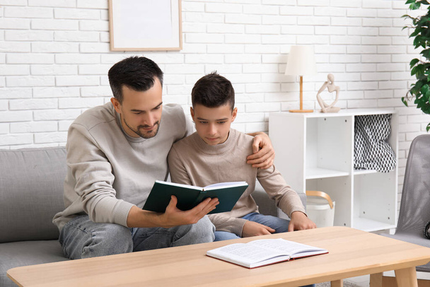 Baba ve küçük oğlu evdeki kanepede kitap okuyorlar. - Fotoğraf, Görsel
