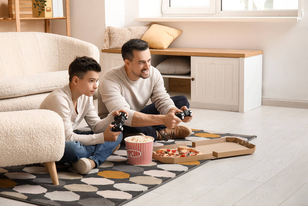 Buon padre e il suo piccolo figlio con cibo gustoso giocare ai videogiochi a casa - Foto, immagini