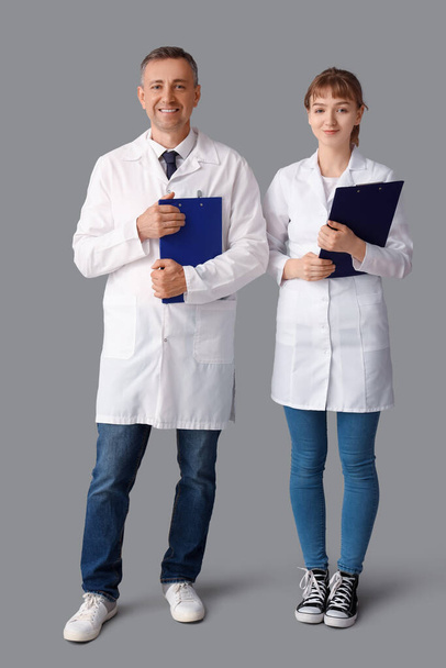 Rijpere arts en zijn assistent met klemborden op lichte achtergrond - Foto, afbeelding