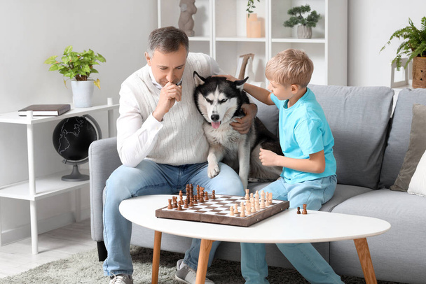 Reifer Arzt mit kleinem Sohn und Hund beim Schachspielen zu Hause - Foto, Bild
