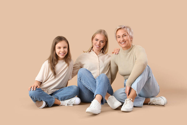 Bambina con la sua mamma e la nonna seduta su sfondo beige - Foto, immagini