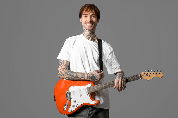 グレーの背景に電気ギターを持つクールな入れ墨された若い男 - 写真・画像