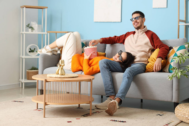 Beau jeune couple heureux avec seau de maïs soufflé regarder la télévision ensemble à la maison - Photo, image