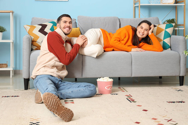 Hermosa joven feliz pareja con cubo de palomitas de maíz viendo la televisión en casa - Foto, imagen