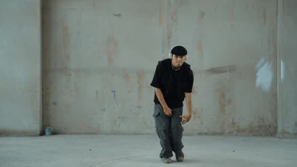 Jóképű hipster gyakorló break tánc közben zenét hallgat fejhallgató cement háttérrel. Mozgókép utcai táncosról, ahogy robottáncol. Kültéri sport 2024. Modern tánc. hiphop. - Felvétel, videó