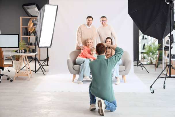 Мужчина-фотограф фотографирует большую семью в студии, вид сзади - Фото, изображение