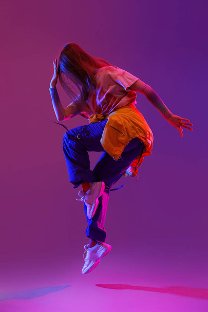 Hermosa mujer joven bailando hip-hop sobre fondo púrpura oscuro - Foto, Imagen