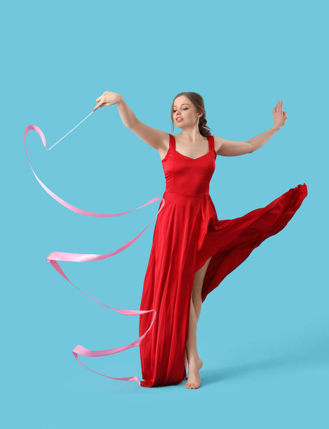 mooie jonge vrouw met lint dansen op blauwe achtergrond - Foto, afbeelding