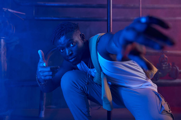 Jovem rapper cara legal posando para câmera em luz de néon. Esportivo millennial menino hip-hop dançarino em estilo de rua elegante roupas retrato - Foto, Imagem