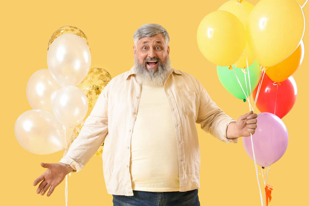 Surpris homme âgé avec des grappes de ballons colorés sur fond jaune - Photo, image