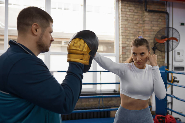 Athletic woman punching to man trainer on taebo training lesson at gym. Sport and female martial arts for self-protection and self-defense concept - Fotó, kép