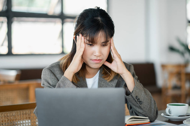 İş kadını iş yerinde stresten bunalmış hissediyor. Kafede dizüstü bilgisayarın önünde el ele tutuşuyor.. - Fotoğraf, Görsel