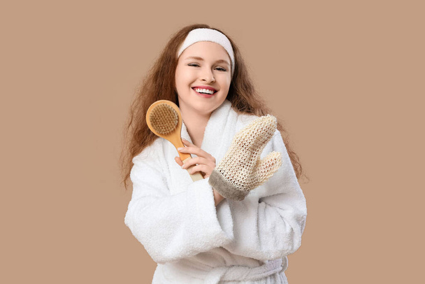 Beautiful young happy woman in bathrobe with bath massage mitten on brown background - Foto, Imagen