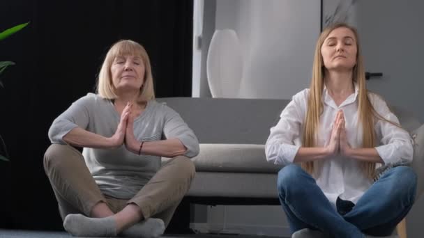 Zwei Frauen sitzen bequem im Schneidersitz mit gefalteten Händen im Gebet und teilen einen Moment des Spaßes und der Verbundenheit. Ihr entspanntes Lächeln zeigt Zufriedenheit - Filmmaterial, Video