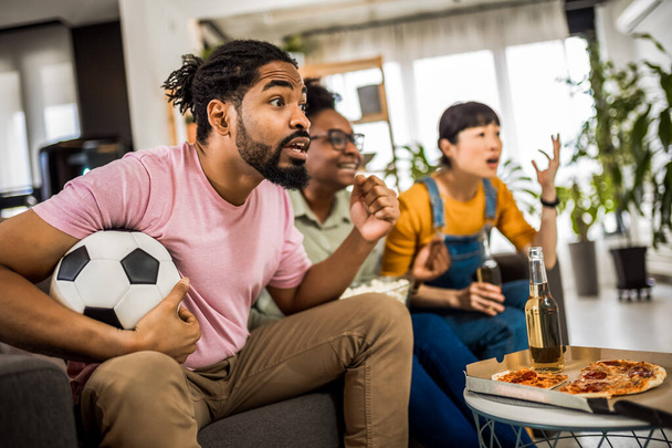 Grupo multirracial de amigos viendo partidos de fútbol, animando, comiendo pizza y bebiendo cerveza. - Foto, imagen