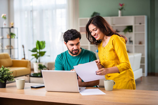 Feliz joven pareja casada india sentarse en la mesa calcular los gastos utilizar fácil servicio de banca en línea en casa - Foto, Imagen