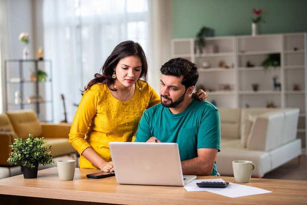 Szczęśliwy młody indyjski małżeństwo siedzieć na stole obliczyć wydatki korzystać z łatwej bankowości online w domu - Zdjęcie, obraz