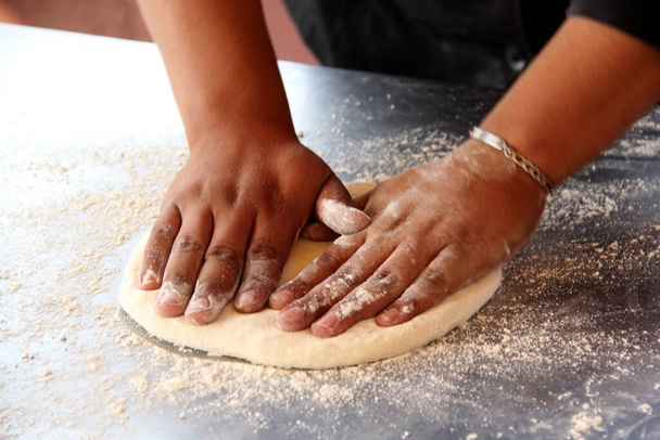 Hands of pizza maker man kneads dough, prepares and shapes for pizza base with rolling pin and flour - Photo, Image