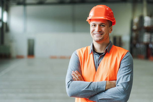 Handsome, man, foreman, construction wearing workwear and hard hat, looking at camera with crossed arms, copy space in warehouse. Concept of industry, advertisement - Photo, Image