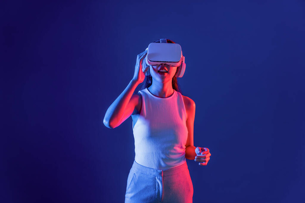 Slimme vrouw staan in cyberpunk neon licht dragen VR headset aansluiten metaverse, futuristische cyberspace community technologie. Elegante vrouw opgewonden zien gegenereerd virtueel landschap. Hallucinatie. - Foto, afbeelding