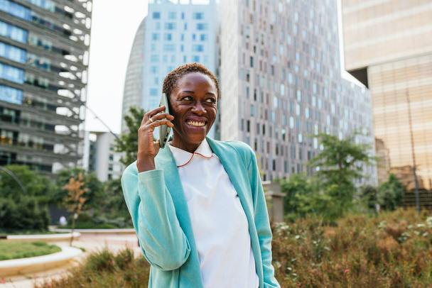 Mulher afro-americana alegre conversando no smartphone em meio a paisagem urbana - Foto, Imagem