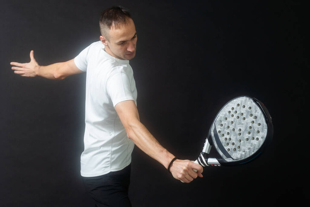 Portré férfi játszik lapát tenisz a helyzetben, hogy elérje a fonák labda fekete elszigetelt háttér. Előre nézz. Kiváló minőségű fénykép - Fotó, kép