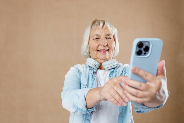 Θετική ευτυχισμένη ηλικιωμένη γυναίκα που φοράει casual ρούχα ποζάρει για selfie κρατώντας smartphone στο ένα χέρι. Έννοια ενεργού γήρατος - Φωτογραφία, εικόνα
