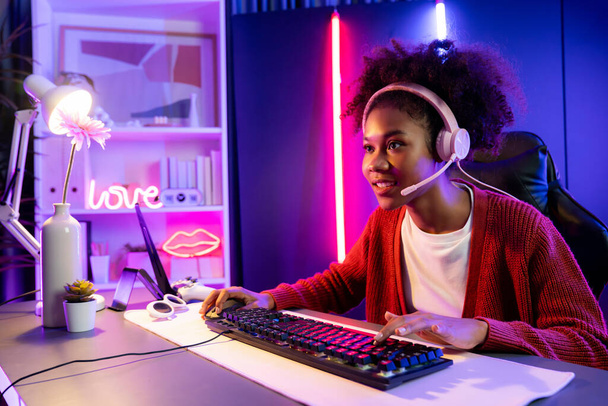 Afrikkalainen amerikkalainen tyttö serpentiini pelaa verkossa taistelevat Esport ammattitaitoinen joukkue yllään kuulokkeet neon väri valaistus huone. Puhuminen muut pelaajat höyläys strategioita voittaa kilpailijoita. Maustevalmistaja. - Valokuva, kuva