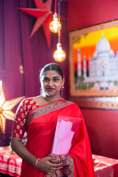 Яскраво усміхнена індійська жінка стоїть перед яскраво-кольоровим святковим тлом. - Фото, зображення