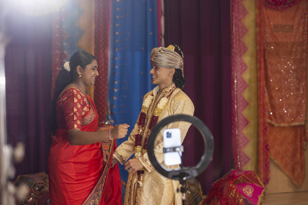 Une jeune femme dans un saree et un homme dans un sherwani échangent des salutations dans une chambre décorée de façon festive. - Photo, image