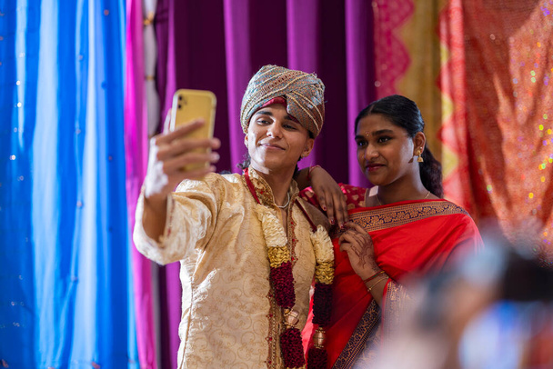 Живая и радостная, молодая индийская женщина запечатлевает свою элегантность в красной сари с селфи на смартфоне. - Фото, изображение