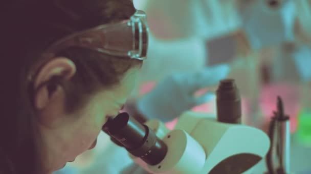 επιστήμονας μελετά εντατικά ένα δείγμα μέσω μικροσκοπίου σε εργαστηριακό περιβάλλον - εστιασμένος ερευνητής εξοπλισμένος με γυαλιά ασφαλείας, αντιπροσωπεύοντας την ακρίβεια στην επιστημονική έρευνα και εκπαίδευση - Πλάνα, βίντεο