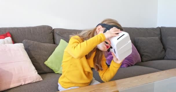 Sechs Jahre altes Kind sitzt zu Hause auf einem braunen Sofa und sieht 360-Grad-Videos mit Virtual-Reality-Brille - Filmmaterial, Video