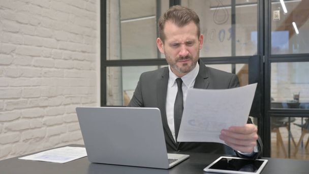 Geschäftsmann mittleren Alters schockiert über Verlust bei der Arbeit an Dokumenten und Laptop - Foto, Bild