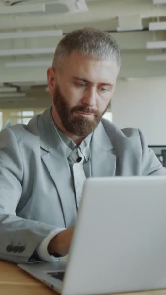 Függőleges lövés üzletember formális öltöny gépelés és az internet használata a laptopon, miközben dolgozik az íróasztal az irodában - Felvétel, videó