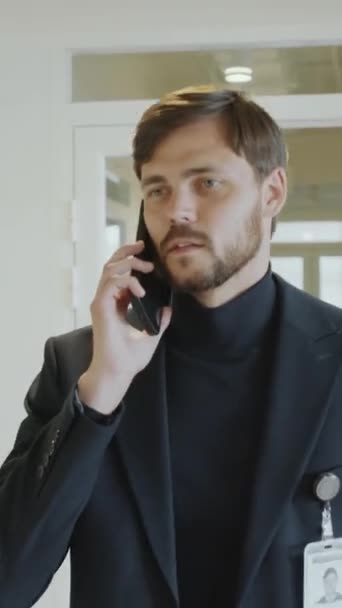 Vertikale Aufnahme eines jungen Geschäftsmannes, der im Büro durch den Flur läuft und Anrufe auf dem Handy entgegennimmt - Filmmaterial, Video