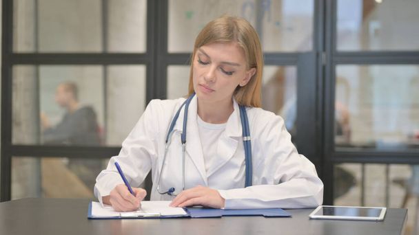 Blond vrouwelijk arts schrijven medisch rapport - Foto, afbeelding
