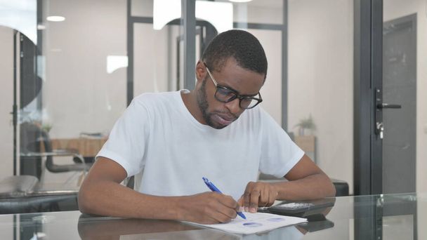 オフィスで文書に取り組んでいる若いアフリカ人男性 - 写真・画像