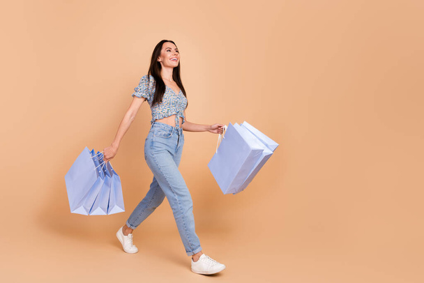 Photo of cheerful positive nice woman wear blue trendy clothes carry packages look blank space isolated on beige color background. - Foto, afbeelding