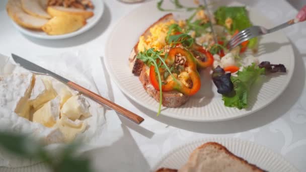 Sluiten van het eten van toast met roerei en gepekelde groenten. Tafel met wit tafelkleed en servies. Hoogwaardige 4k-beelden - Video
