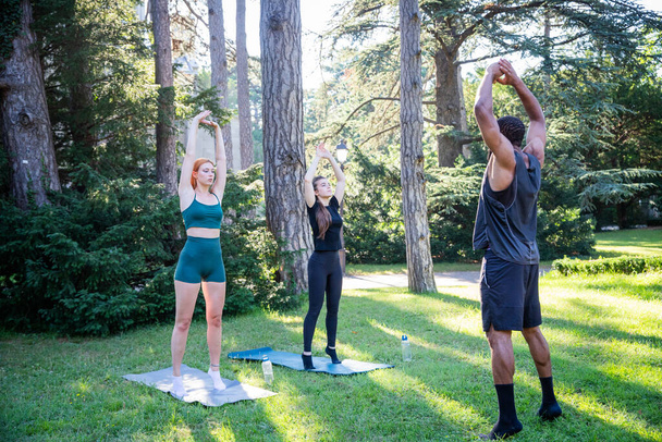 Three sporty people are exercising in a park doing some stretching exercises. - Photo, Image