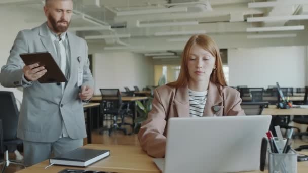 Mladá obchodní dáma pracující na notebooku a diskutující data na digitálním tabletu s mužským spolupracovníkem v moderní open space kanceláři - Záběry, video