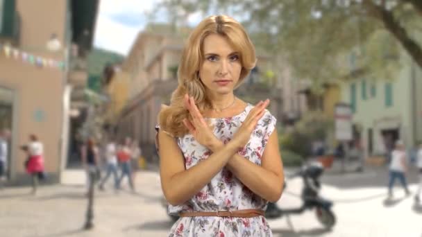 Портрет серьезной блондинки, стоящей на улице, скрещивает руки в знак запрета. Городская улица на заднем плане. - Кадры, видео